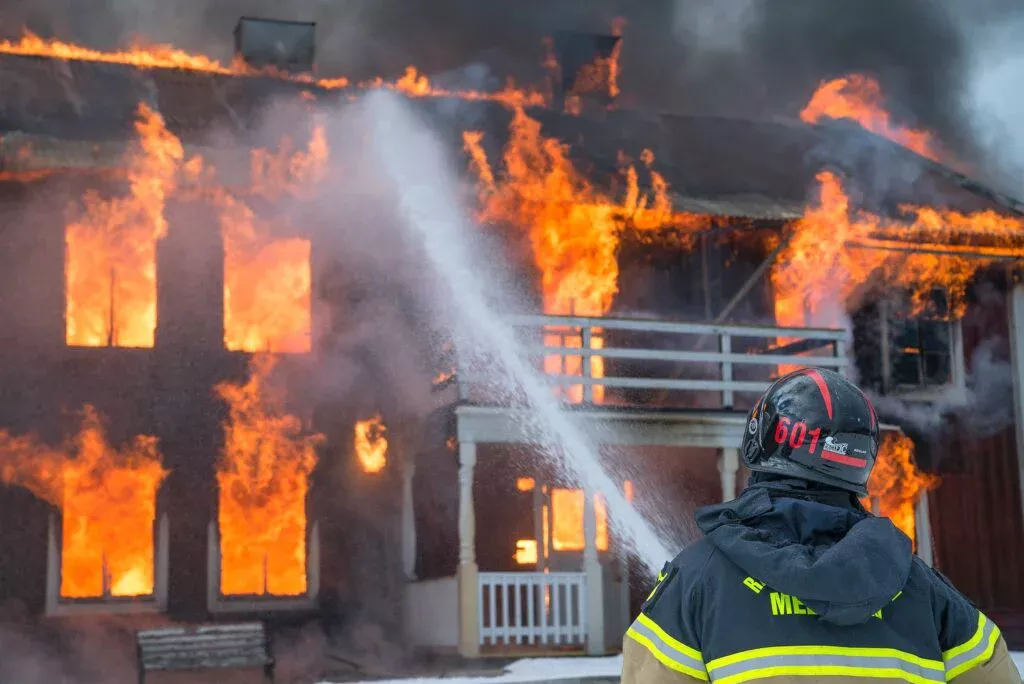 Ett radhus brinner, brandman sprutar vatten med brandslang
